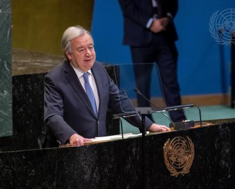 A man inn a dark grey suit and blue tie, the UN Secretary-General, speaks from a podium at the UN building