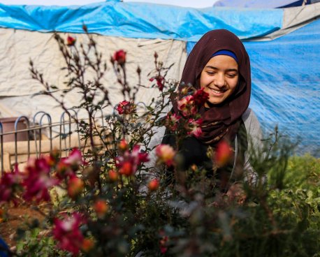 A young woman in Iraq stands in front a small plant.