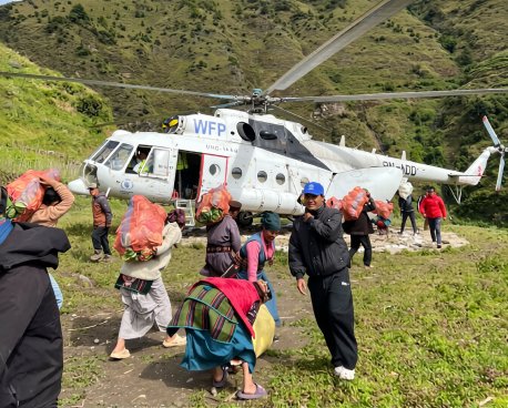 People carry bags of food in Nepal in front of a helicopter.