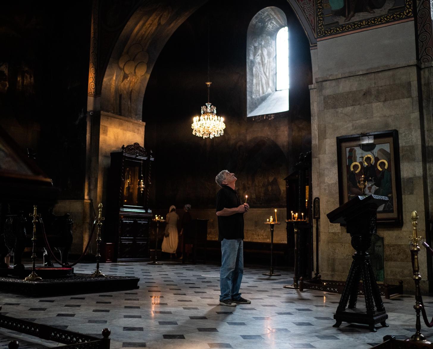 رجل ينظر إلى الأعلى حاملاً شمعة في مكان عبادة.