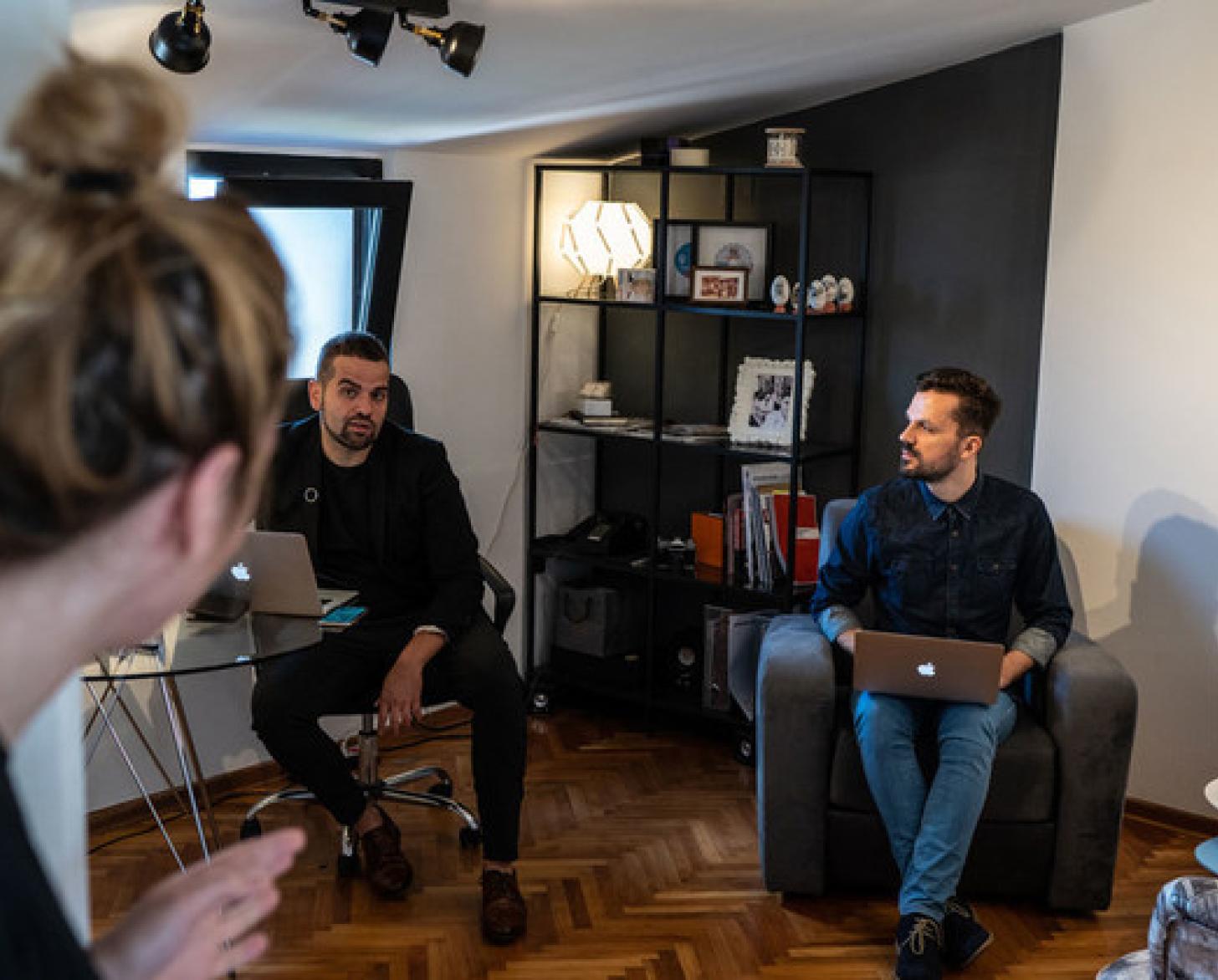 رجلان يمسكان أجهزة الكمبيوتر المحمولة الخاصة بهما أثناء التحدث مع امرأة ومع بعضهما البعض.