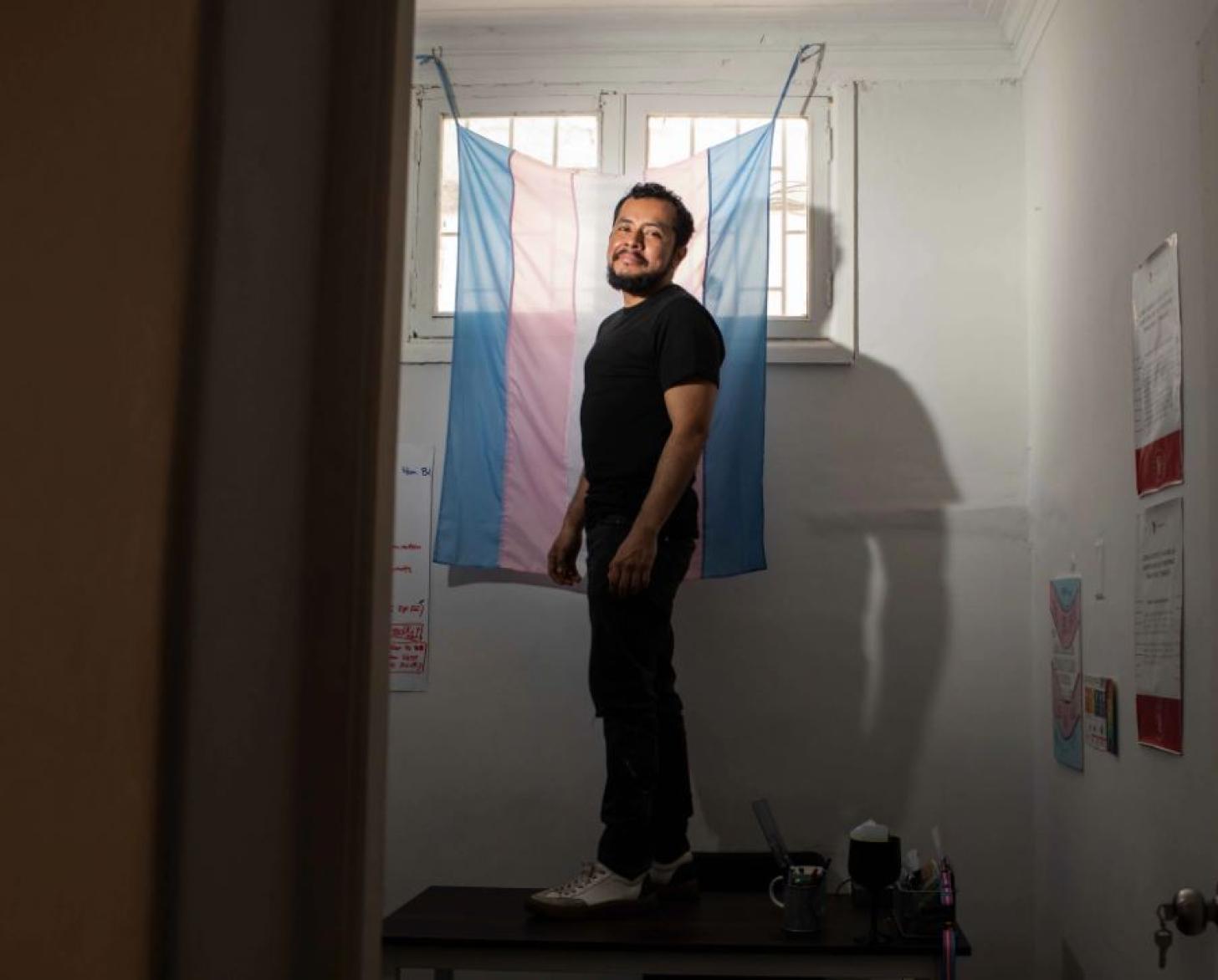 Photo shows Marco standing atop a desk, as he stands in front of a flag draped over a window.