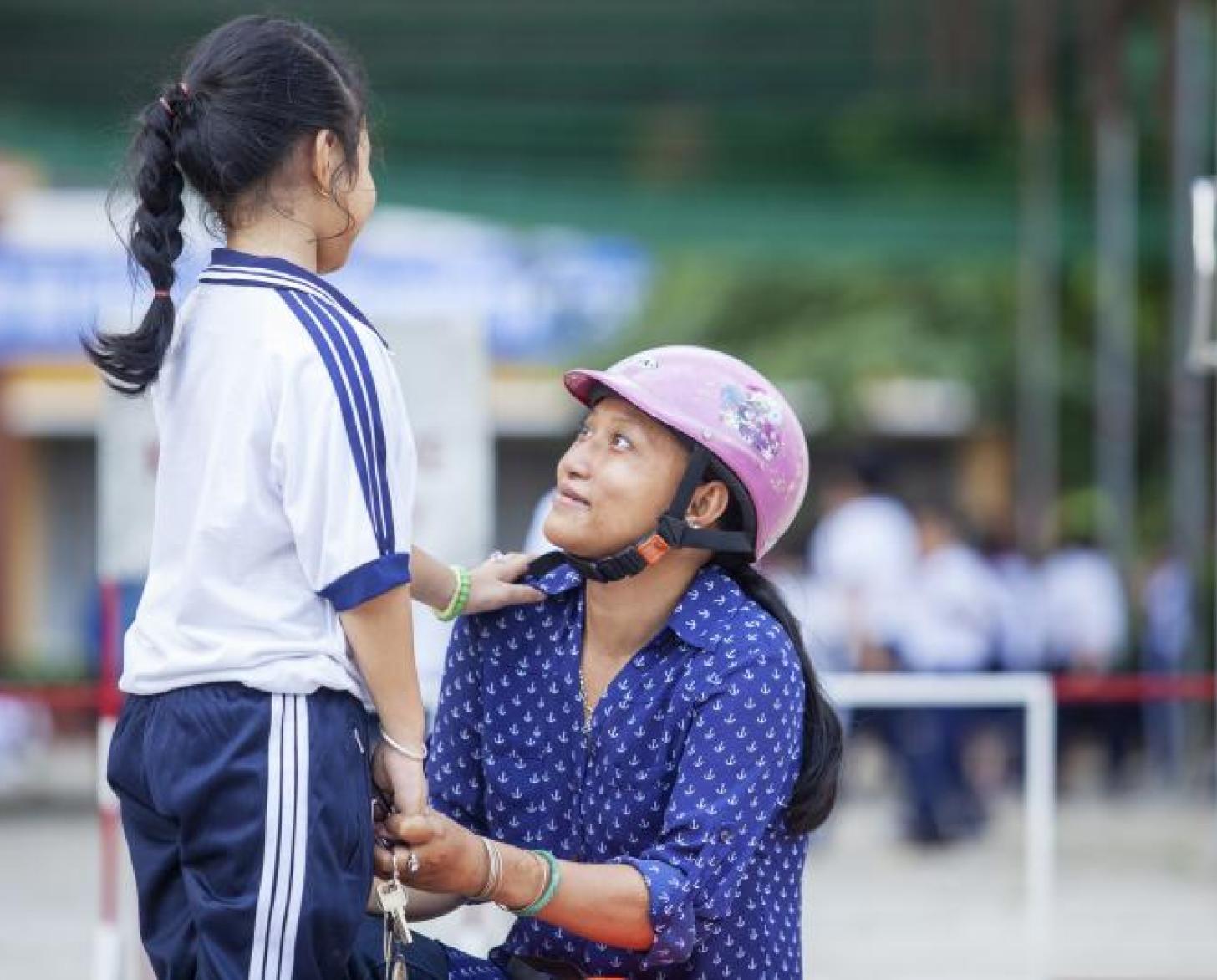 تشاو باو ترتدي خوذة، تجثو على ركبتيها وهي تنظر بحنان إلى ابنتها.