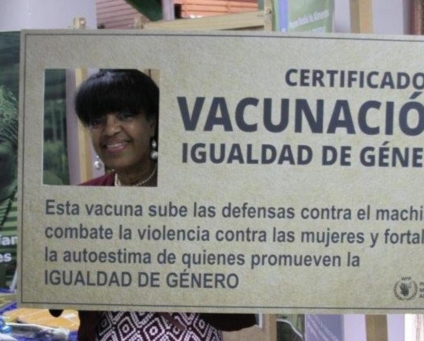 Yudith stands with her head in a cut of a giant-sized gender equality certificate.