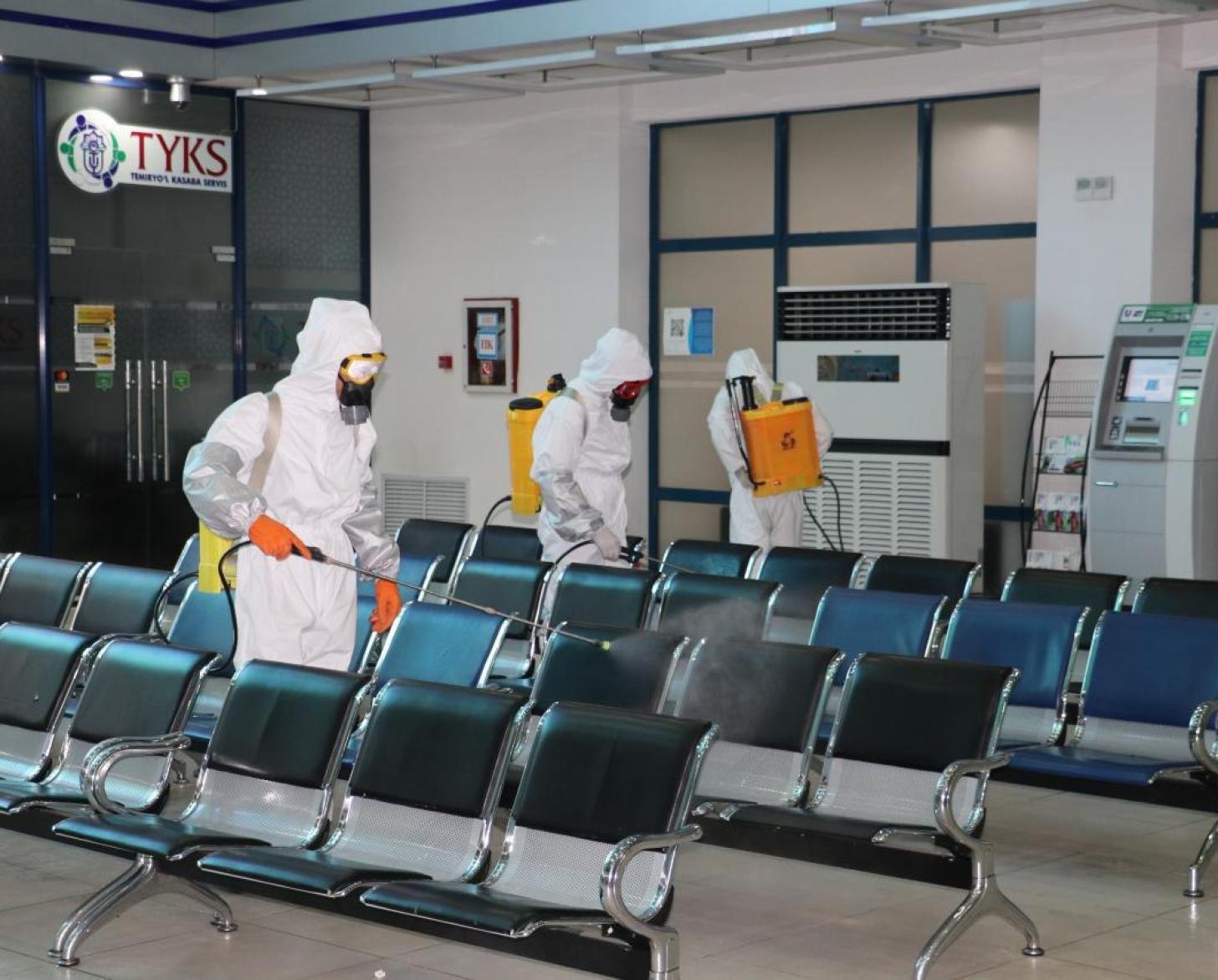 أشخاص يرتدون ملابس واقية من الرأس إلى أخمص القدمين ويقومون بتنظيف وتعقيم منطقة الانتظار.