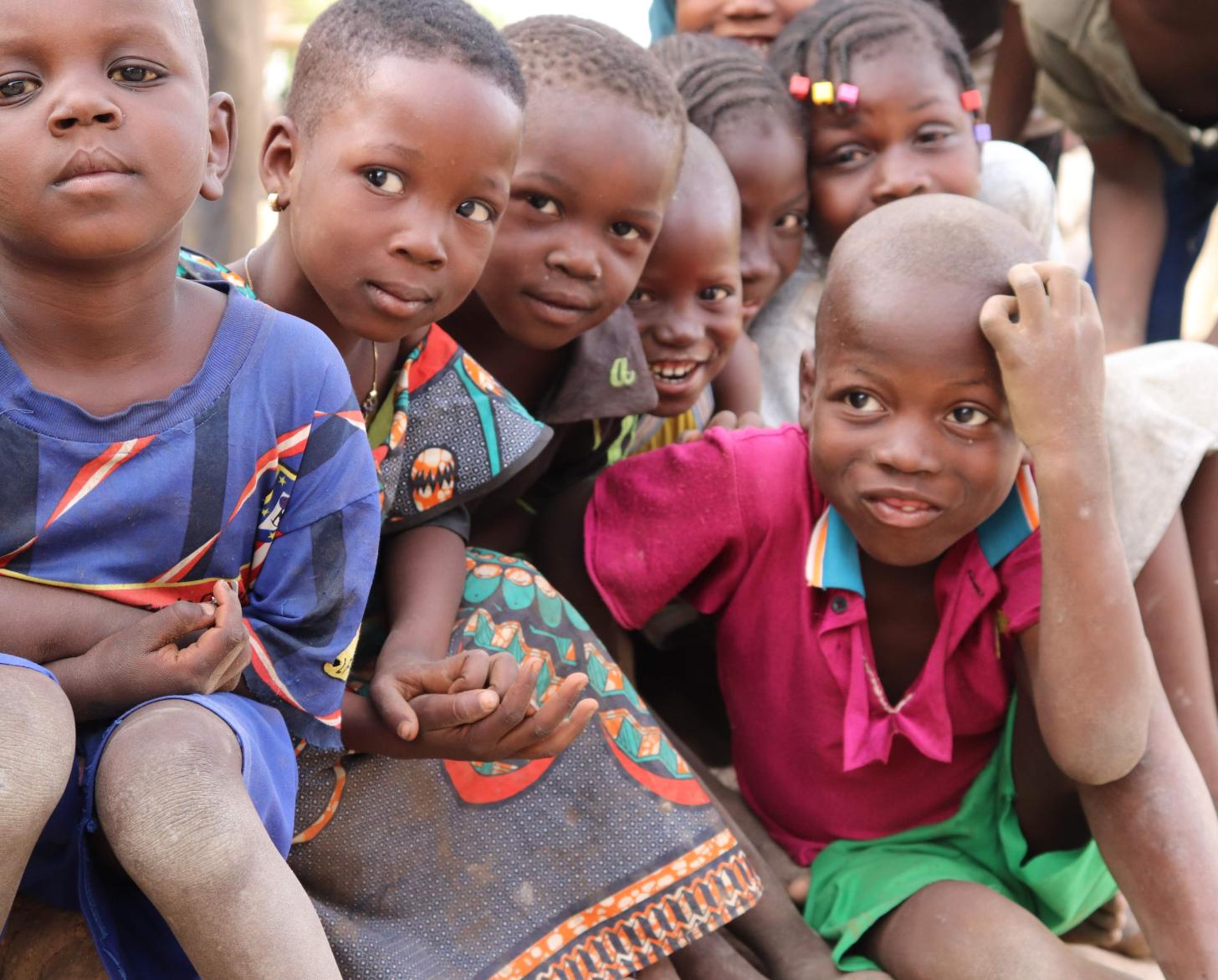 Young children sit together and look curiously at the camera. Birth certificates help ensure these and other children are not left behind.