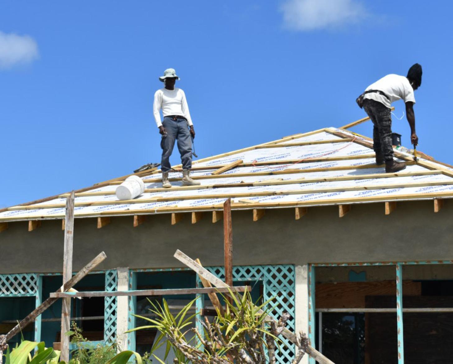 Deux hommes travaillent à la reconstruction d'une maison endommagée par une catastrophe naturelle. Ils se tiennent tous les deux sur le toit en bois de la maison.