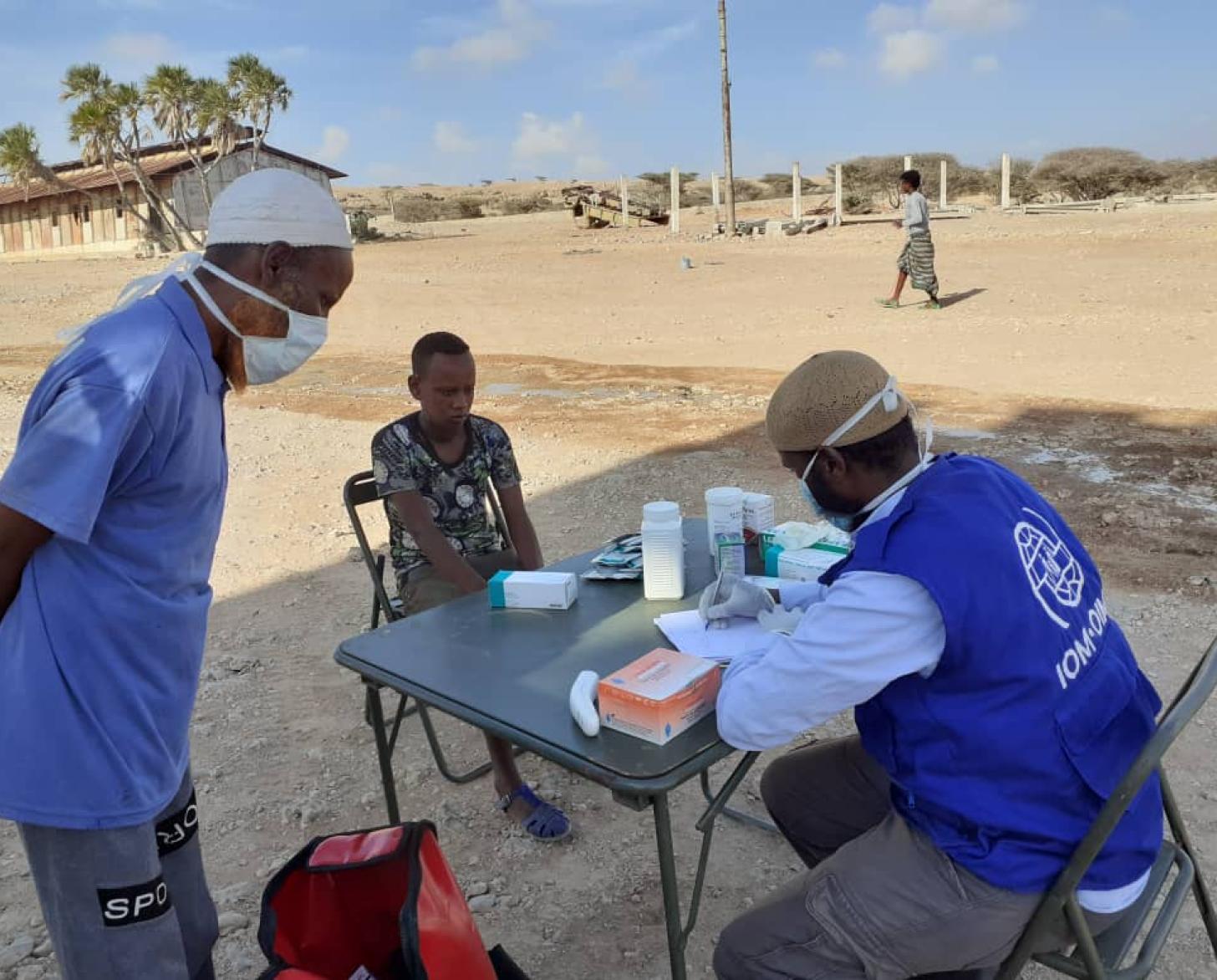 يجلس موظفو الأمم المتحدة والنساء معًا بينما يقوم الموظف بتدوين الملاحظات ويقف بجانبه رجل يرتدي قناعًا.