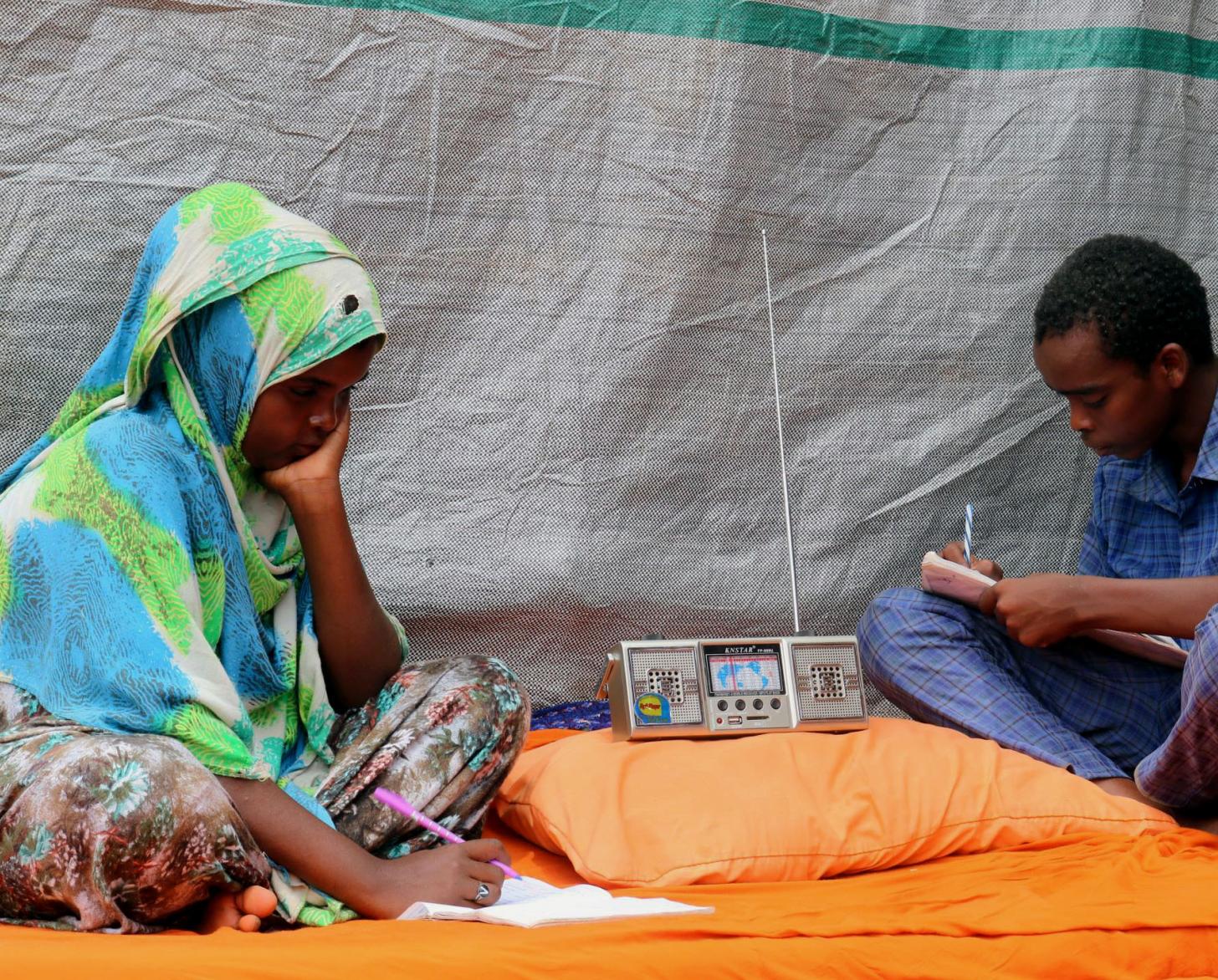 شاب وشابة يجلسان بجوار راديو محمول ويكتبان.