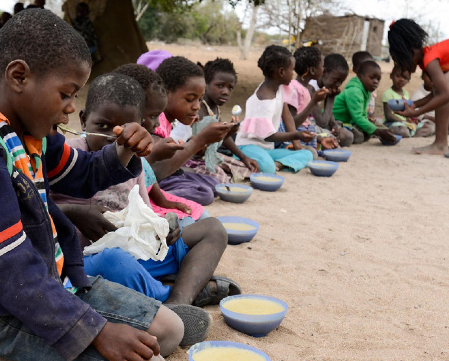 Niños y niñas sentados al aire libre mientras comen en la escuela de la provincia de Maputo, en Mozambique.