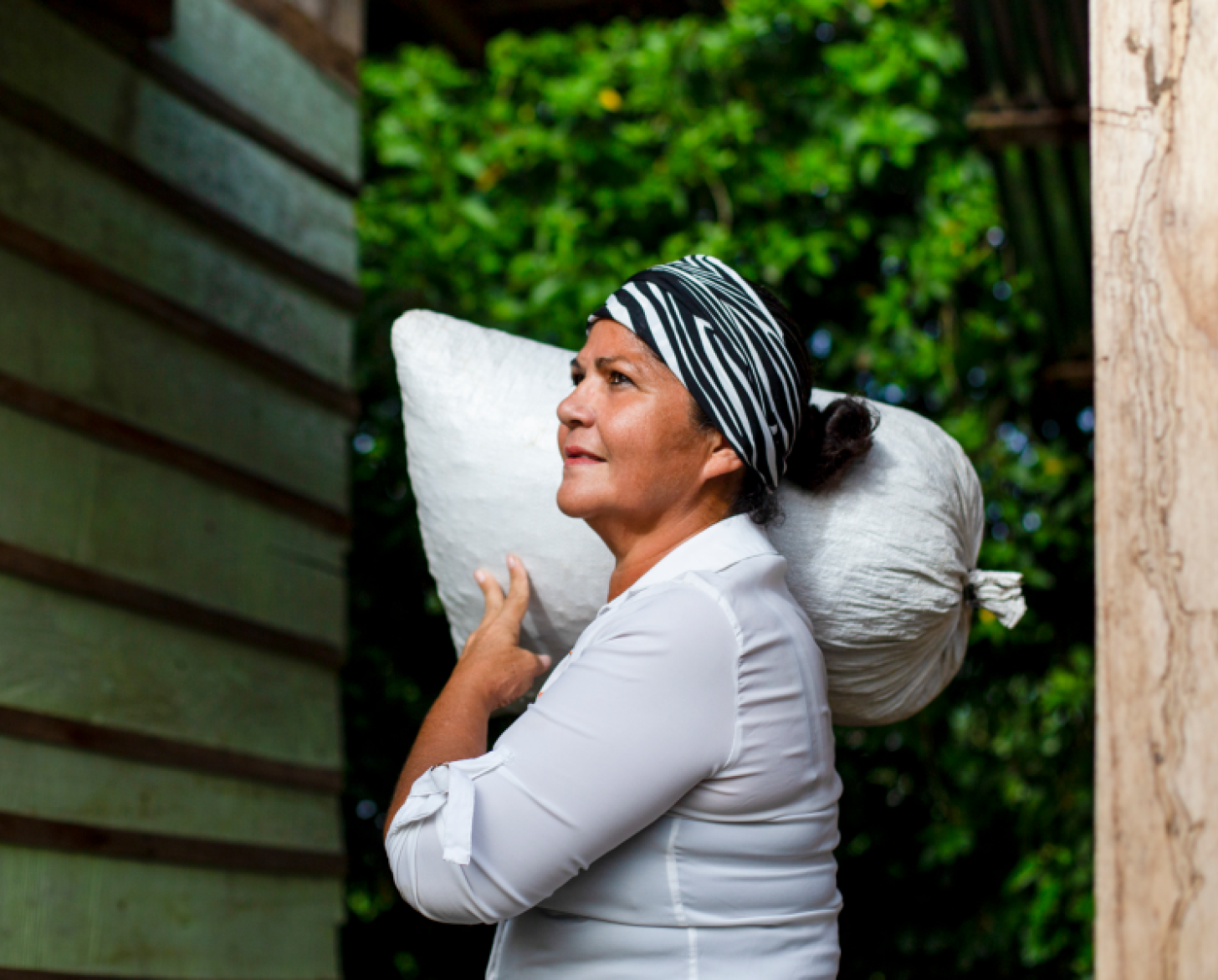 A woman looks up stoically as she holds a large bag over her shoulders.