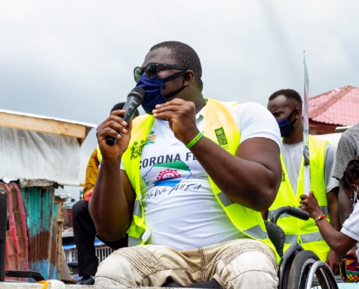A photo of George Wyndham, a Paralympic medalist from Sierra Leone, in his wheelchair and speaking into a microphone to address a crowd