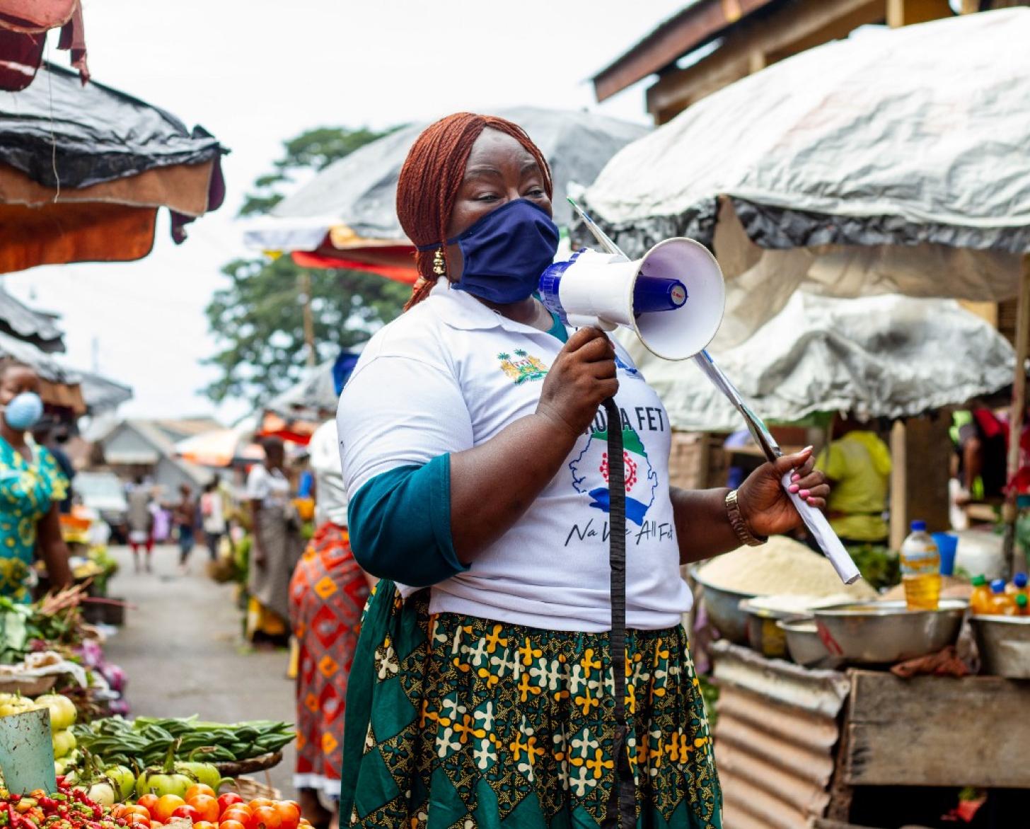 A community mobilizer speaks into a megaphone while standing in the middle of a market in Sierra Leone