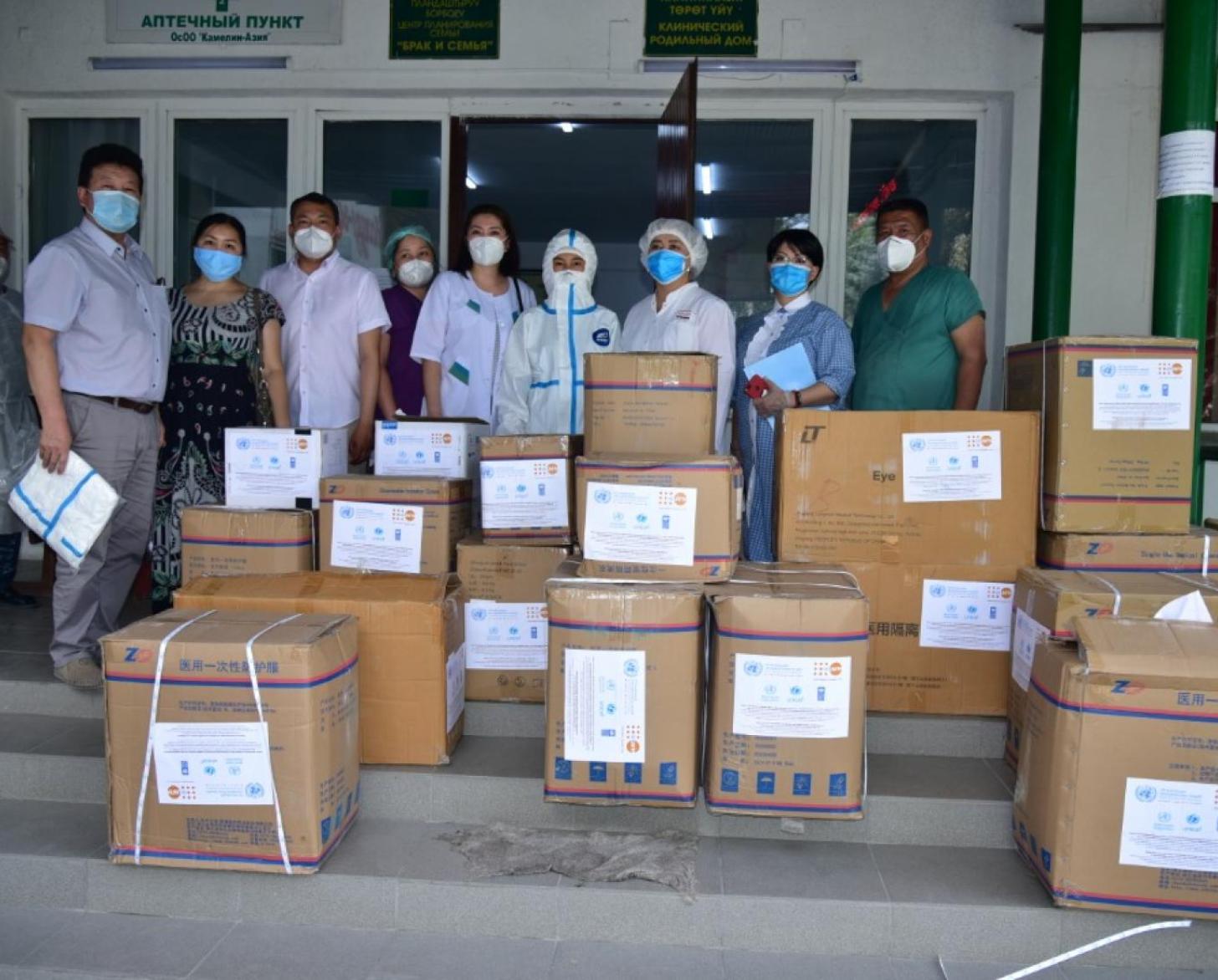 UN personnel and healthcare workers stand behind donation boxes wearing protective gear.