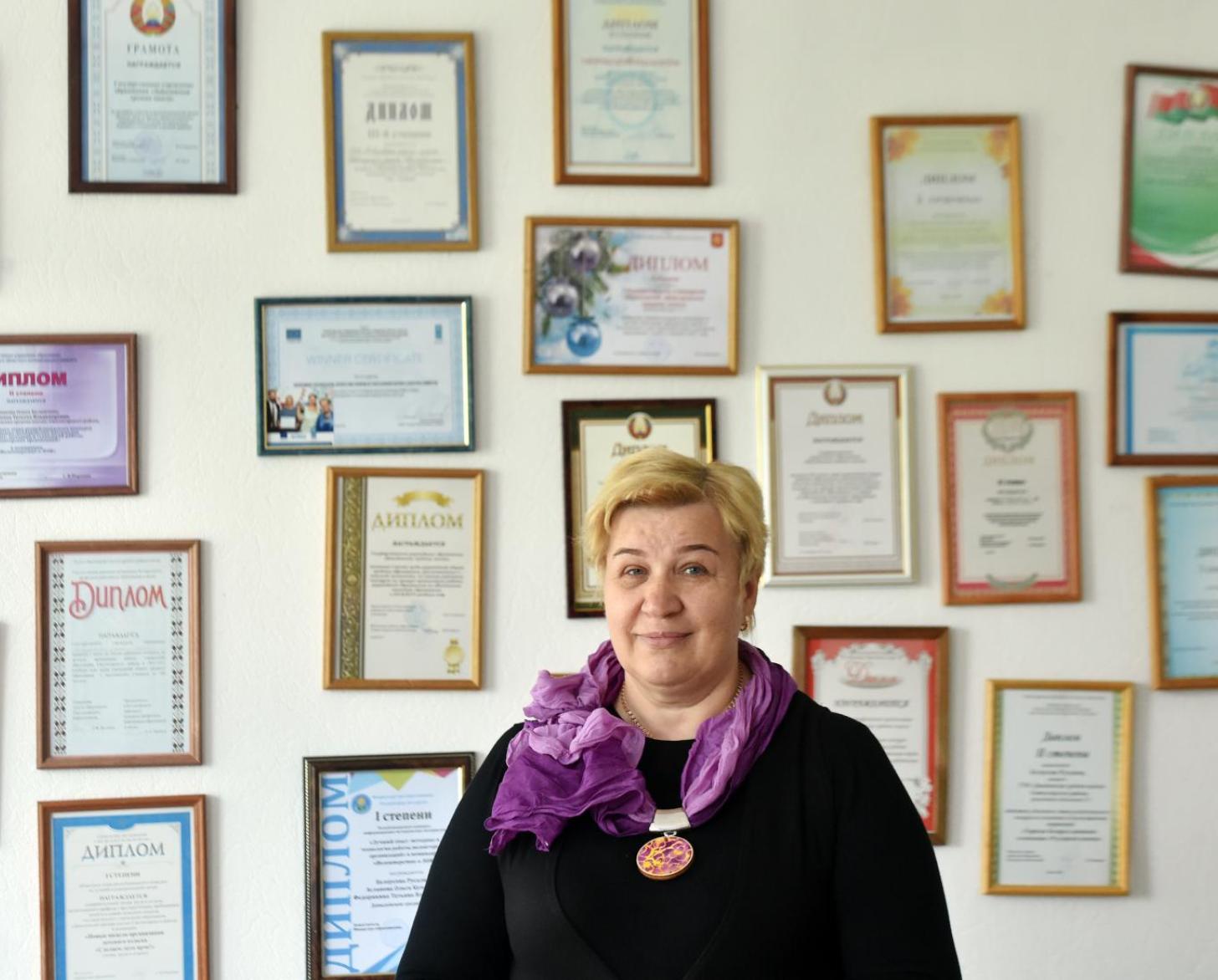 Svetlana Markevich, directora de la Escuela Secundaria Davydovskaya, está orgullosa frente a una pared de certificados y diplomas enmarcados.