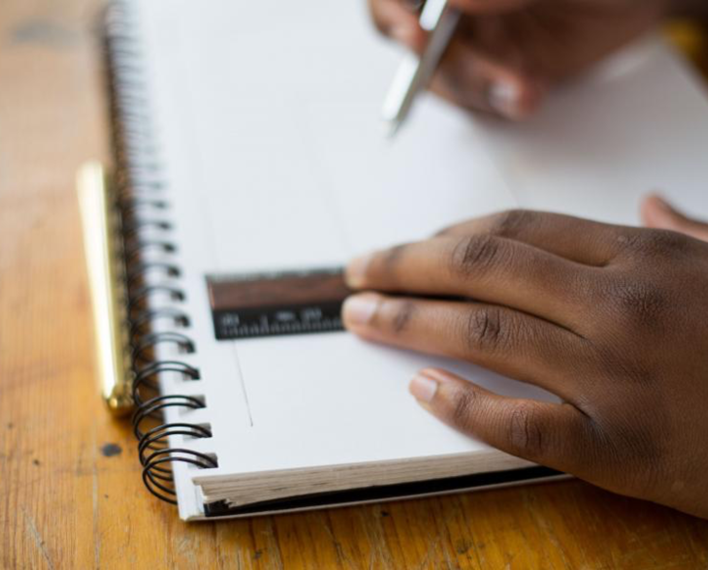 Primer plano de las manos de un niño que sostiene una regla sobre un bloc y un bolígrafo en la otra mano.