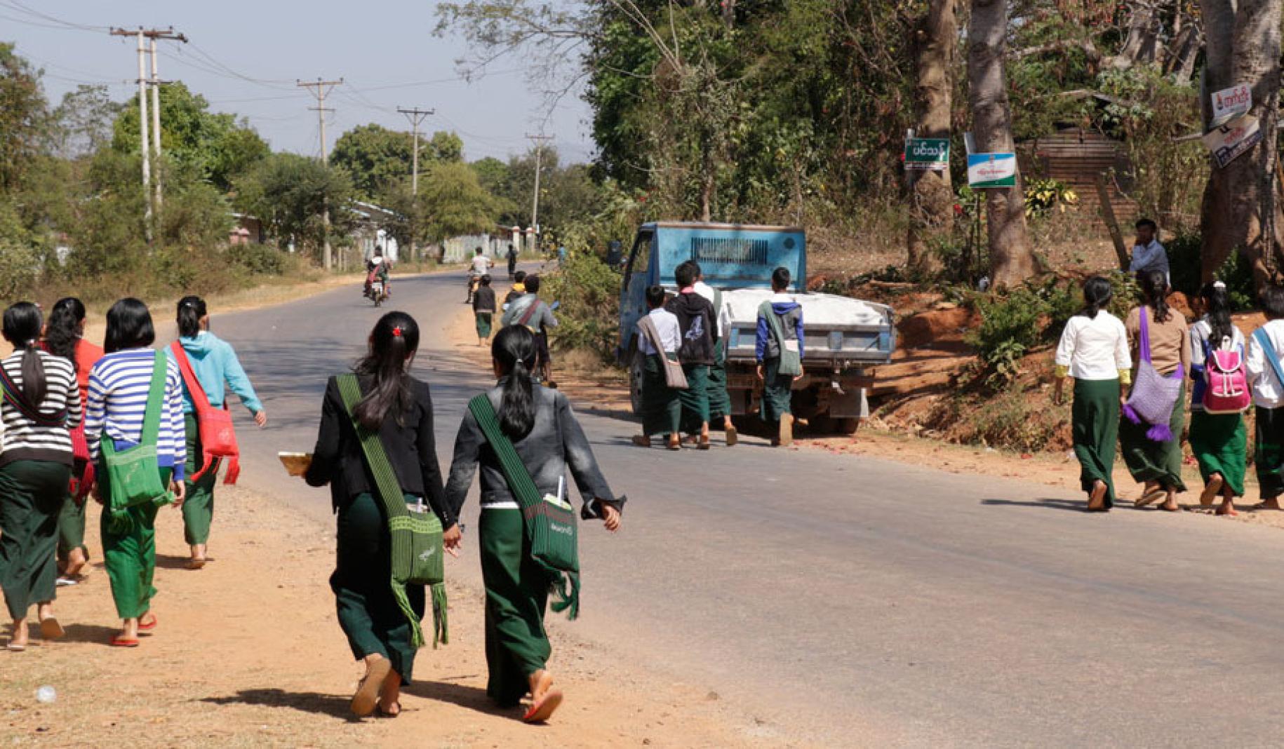Students walking in groups on the side of a rode heading to school.