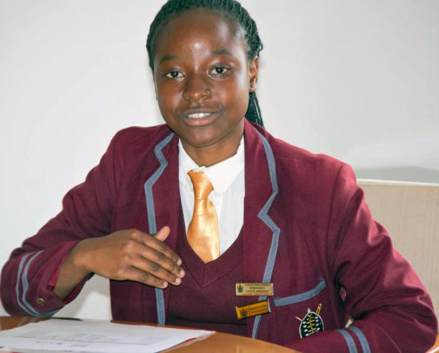 فتاة في المدرسة من زمبابوي ترتدي زيها المدرسي وتجلس على مكتب.