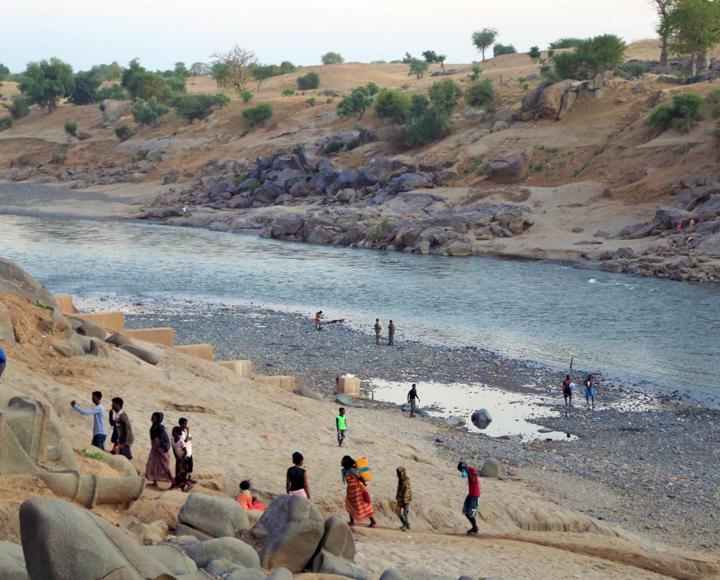 La foto muestra a los refugiados caminando por una zona de agua y subiendo una gran colina.