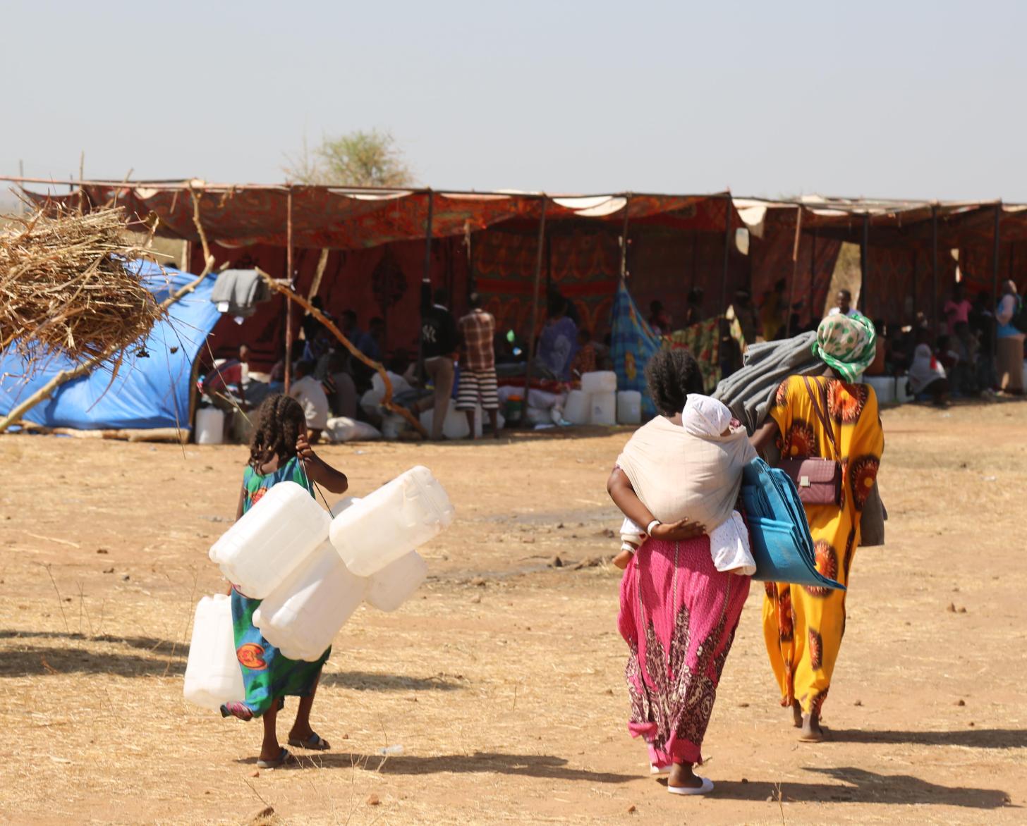 Refugees and migrants carry jugs and supplies near the camp.