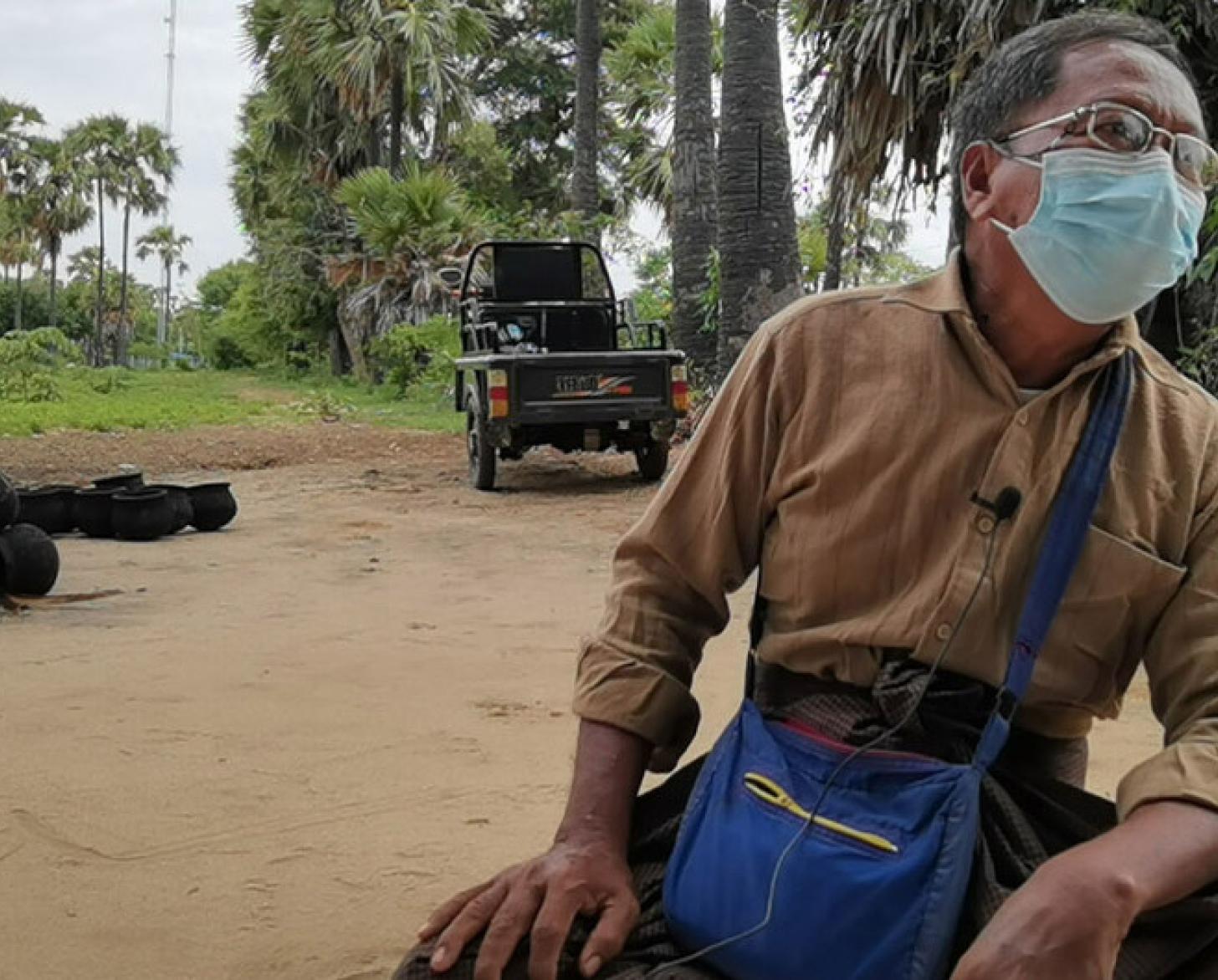 U Cho wearing a face mask sits down in front of the farmland.