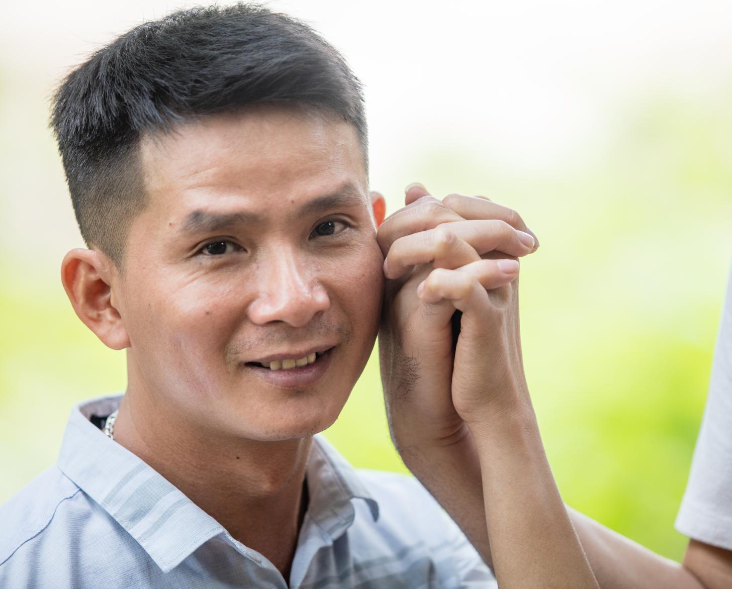 رجل ينظر إلى الكاميرا مبتسمًا بينما يمسك يد حبيبه.