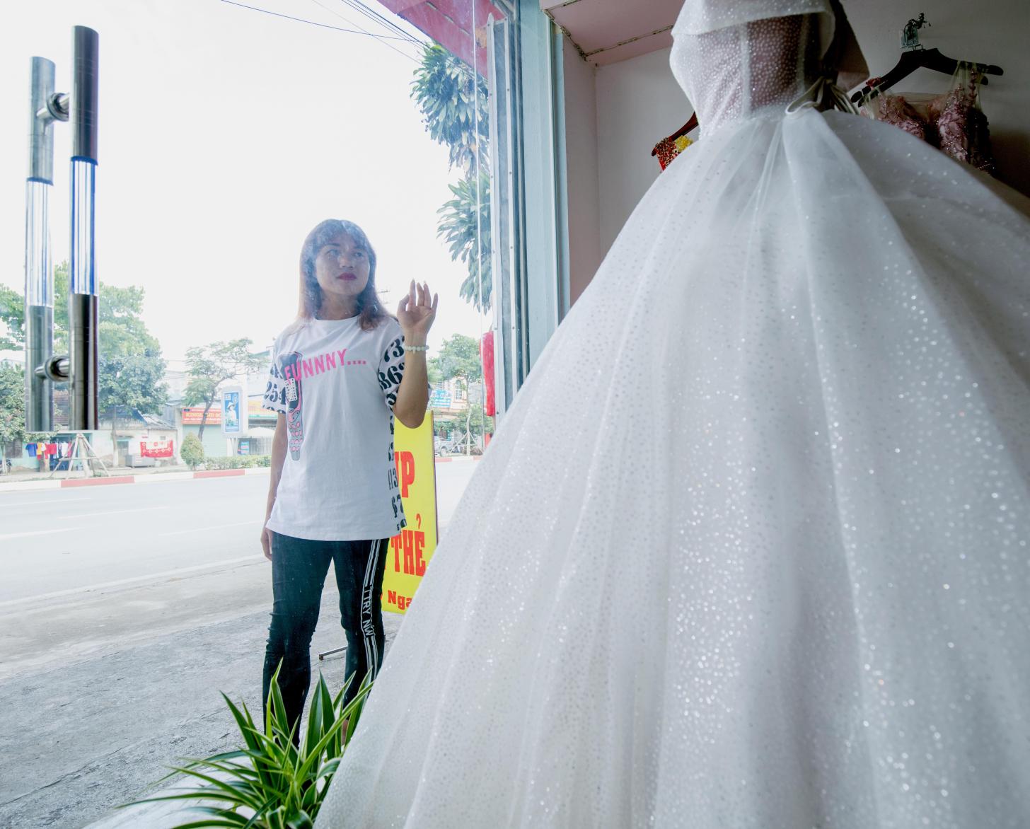 Lo Kim Thuy admires a wedding dress displayed in a store front's window.