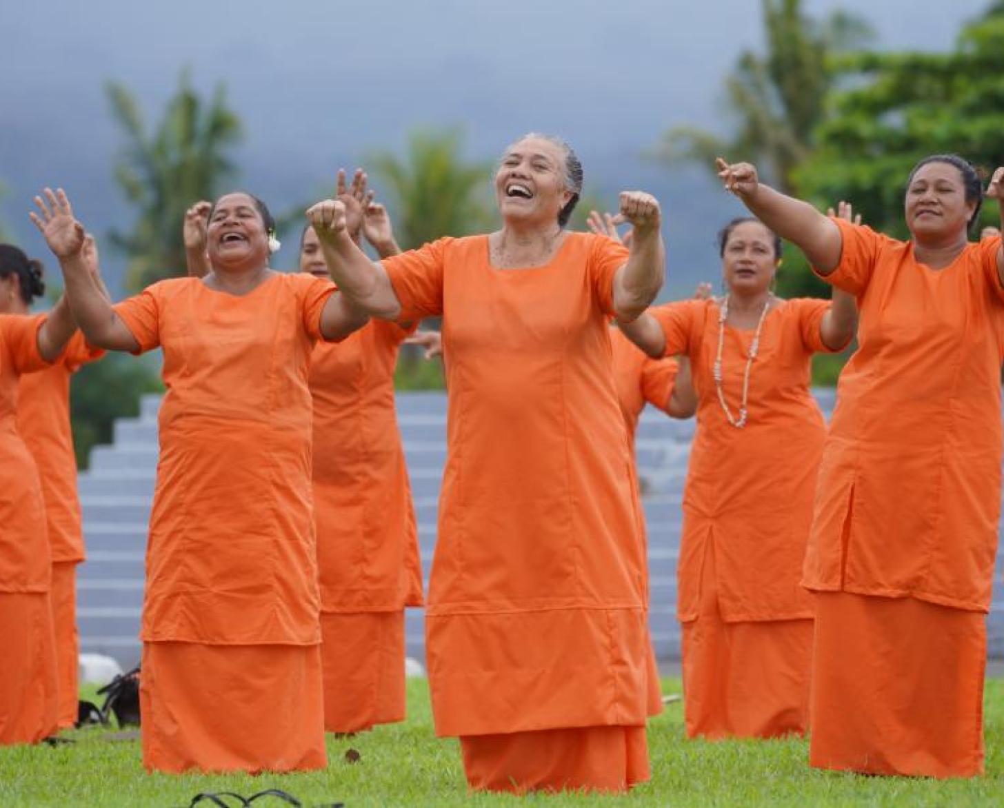Women all dressed in orange perform at a gender-based violence event outside.
