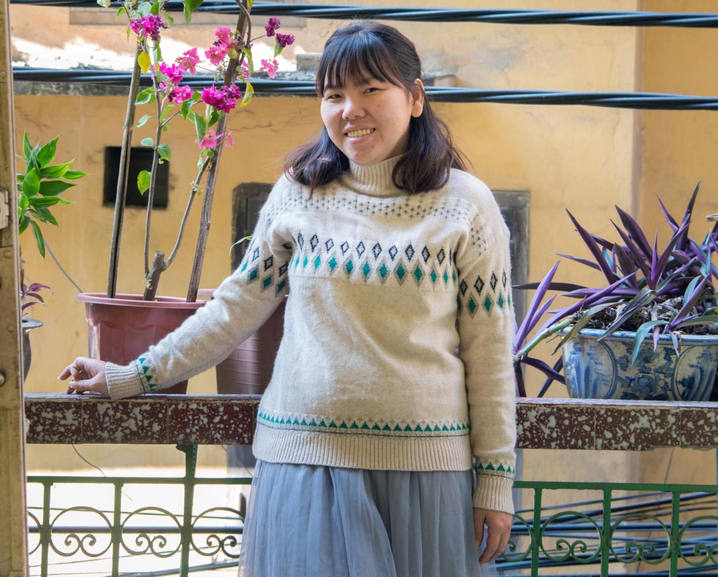 Tu Thanh Thuy stands proudly outside on a porch near a magenta coloured orchid and lilac coloured plants.
