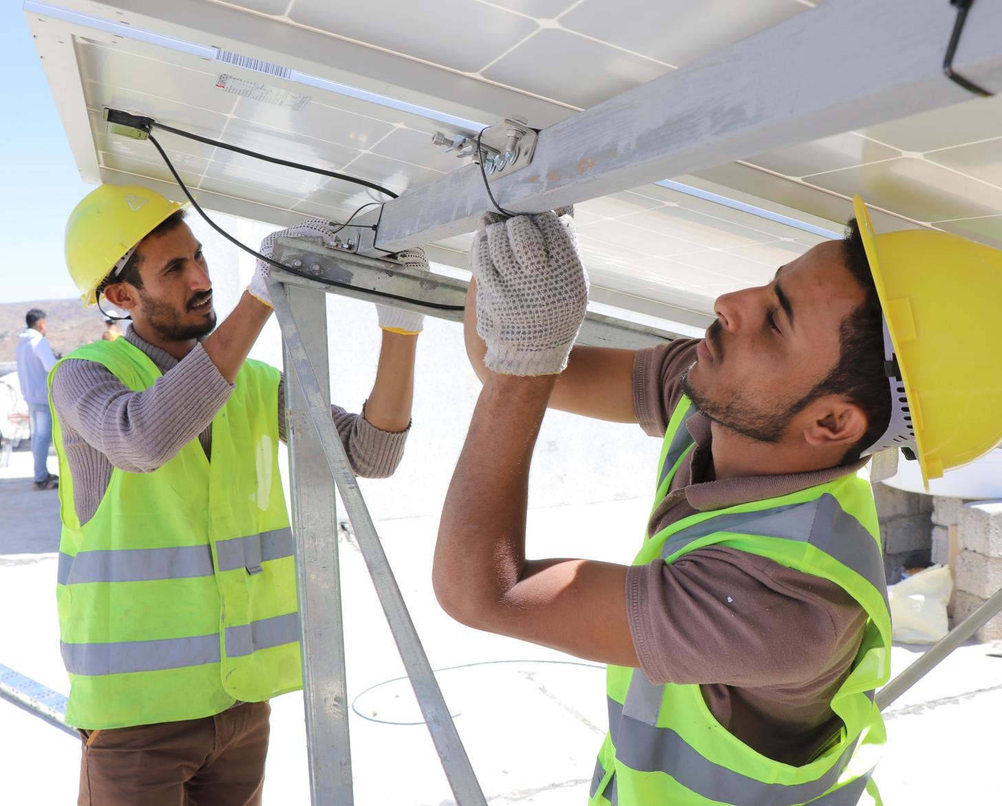 Dos hombres con cascos y chaquetas reflectantes están trabajando en paneles solares.