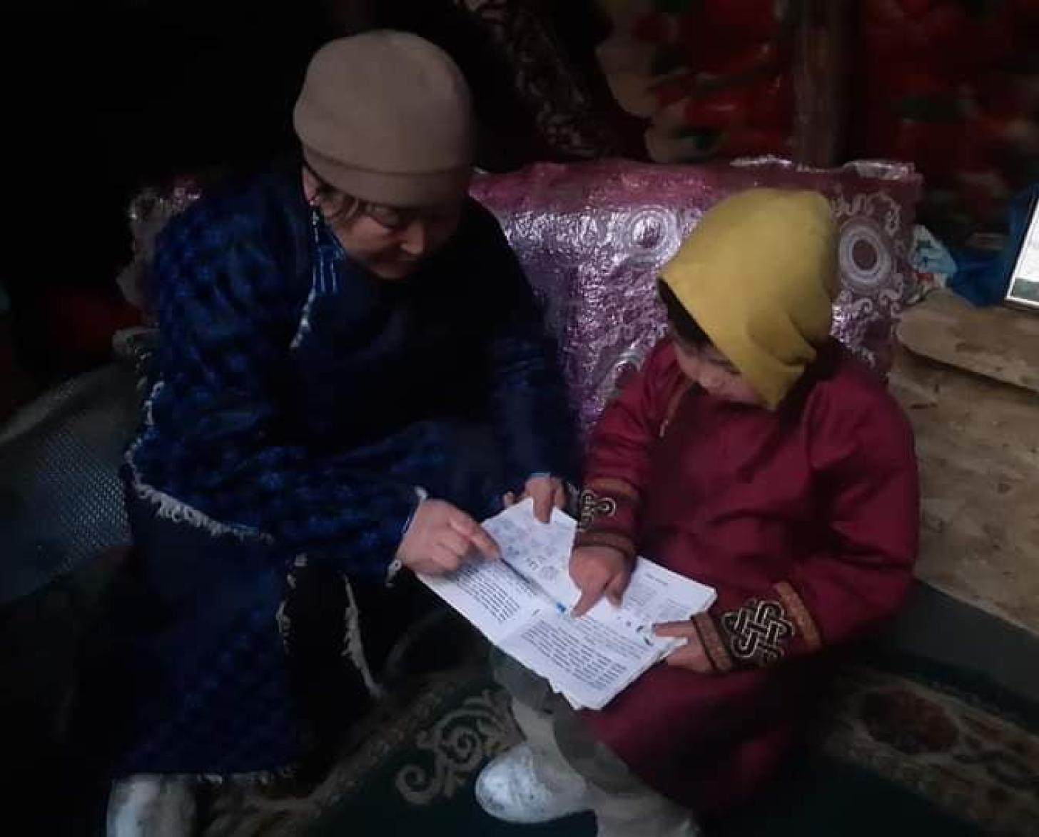 A woman dressed in blue shows a child dressed in red from a piece of paper. 