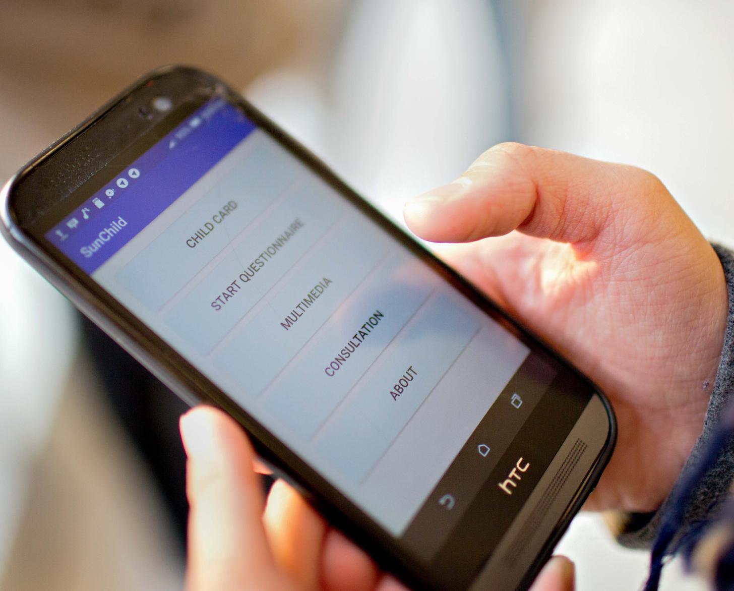 A close-up of a girl's hand holding a mobile phone. The screen displays the SunChild app features.