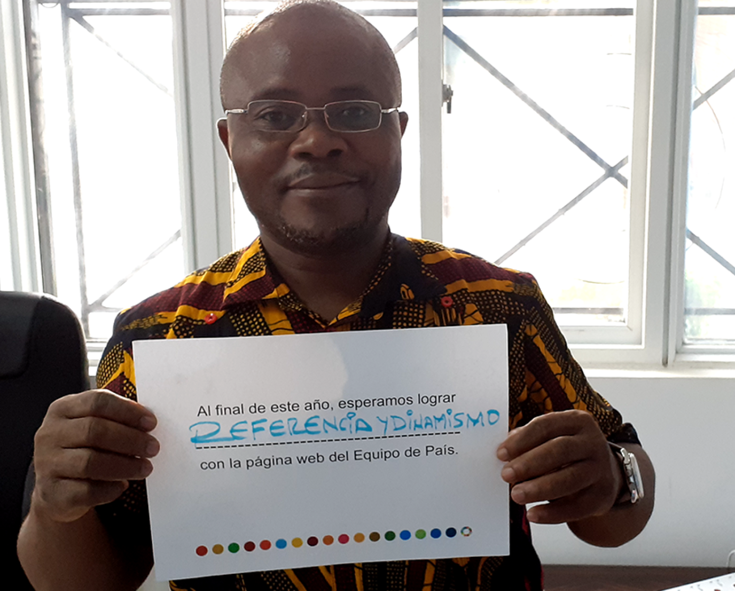 Un hombre con una media sonrisa, que transmite orgullo, sostiene un letrero sobre los objetivos colectivos anuales del equipo de la ONU en el país respecto al nuevo sitio web. "Al final del año, esperamos lograr referencia y dinamismo", destaca el letrero en español.
