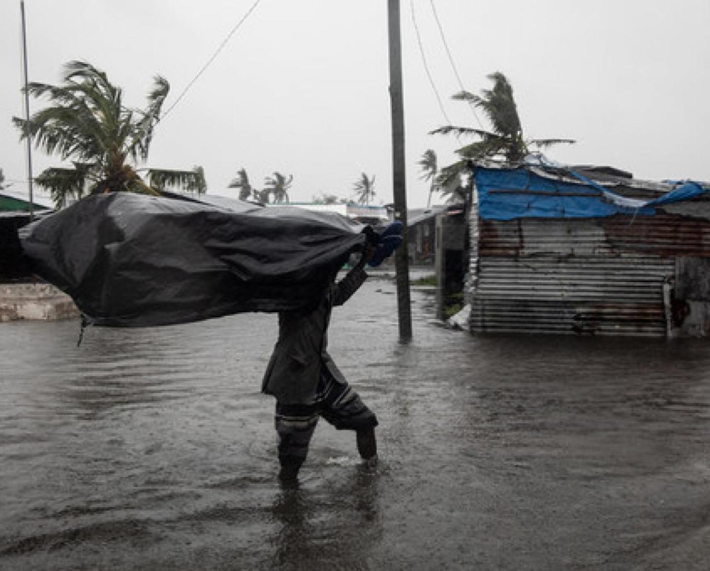 رجل يسير في الحي الذي غمرته المياه ويحمل كيسًا كبيرًا فوق رأسه.