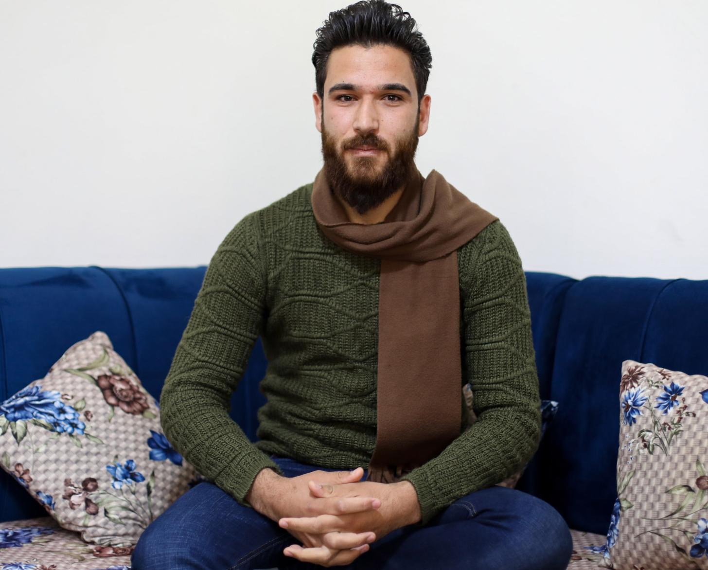 Ammar sits on a sofa with his arms crossed on his lap. 