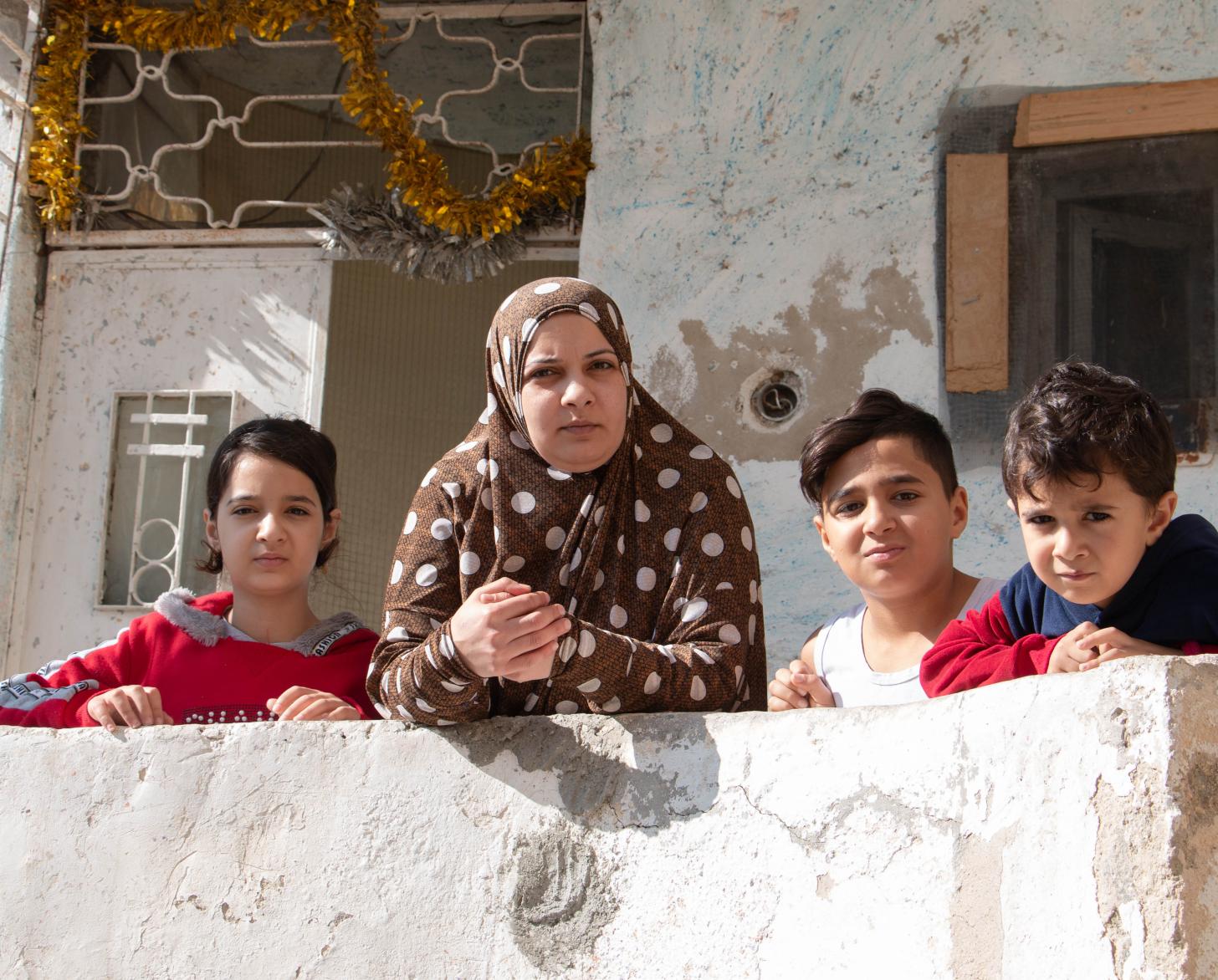 Asma stands with her three children on the porch of their home.