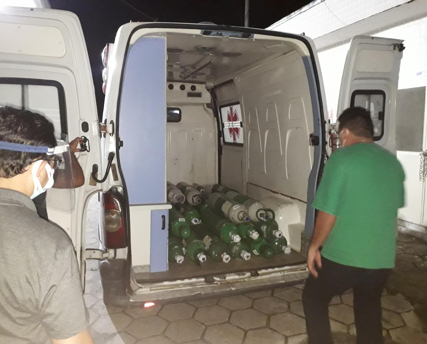 Two men stand near an open trunk of a truck with oxygen tanks. 