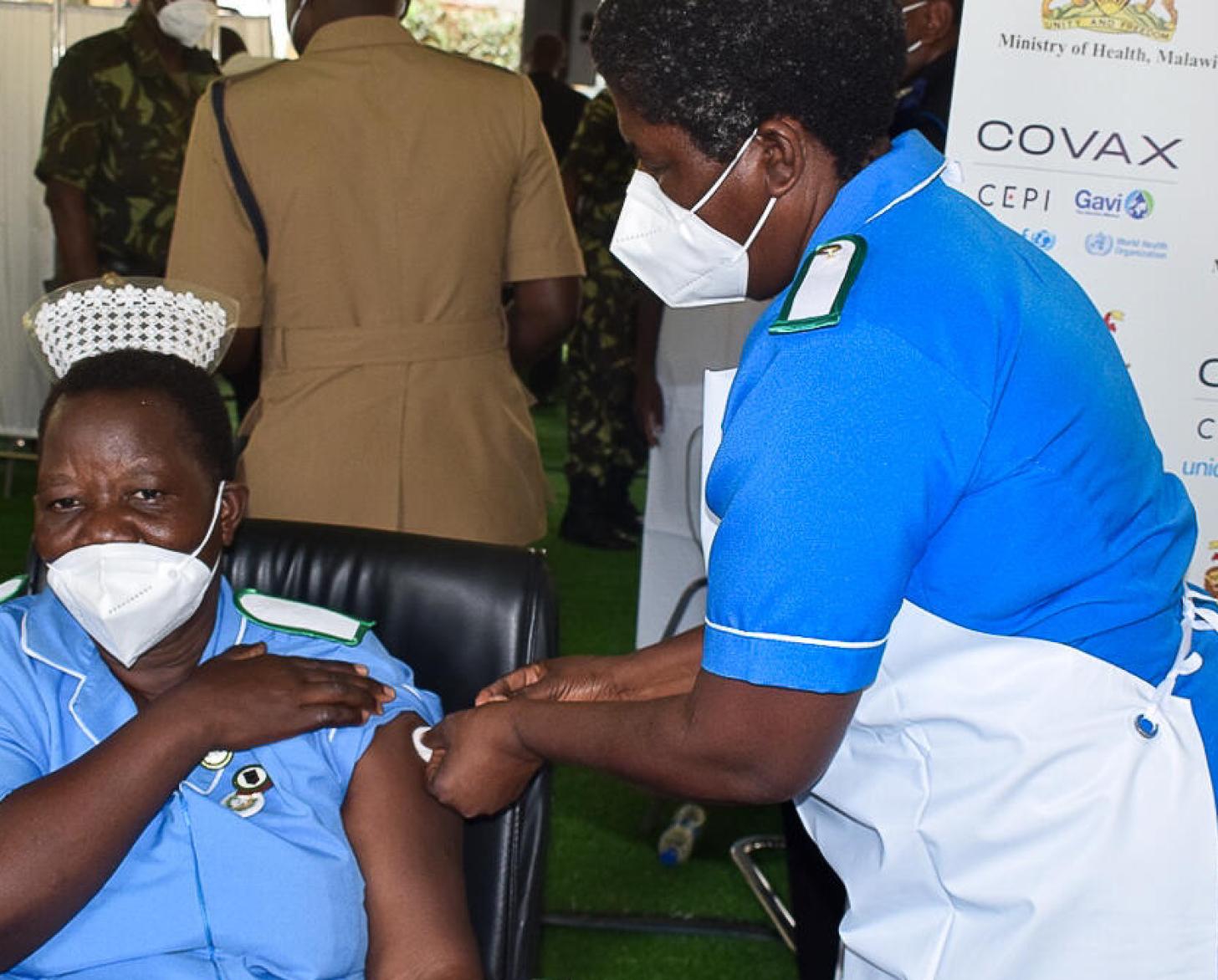 A healthcare professional at a vaccination site rolls up her sleeve as she receives a vaccine administered by her colleague.