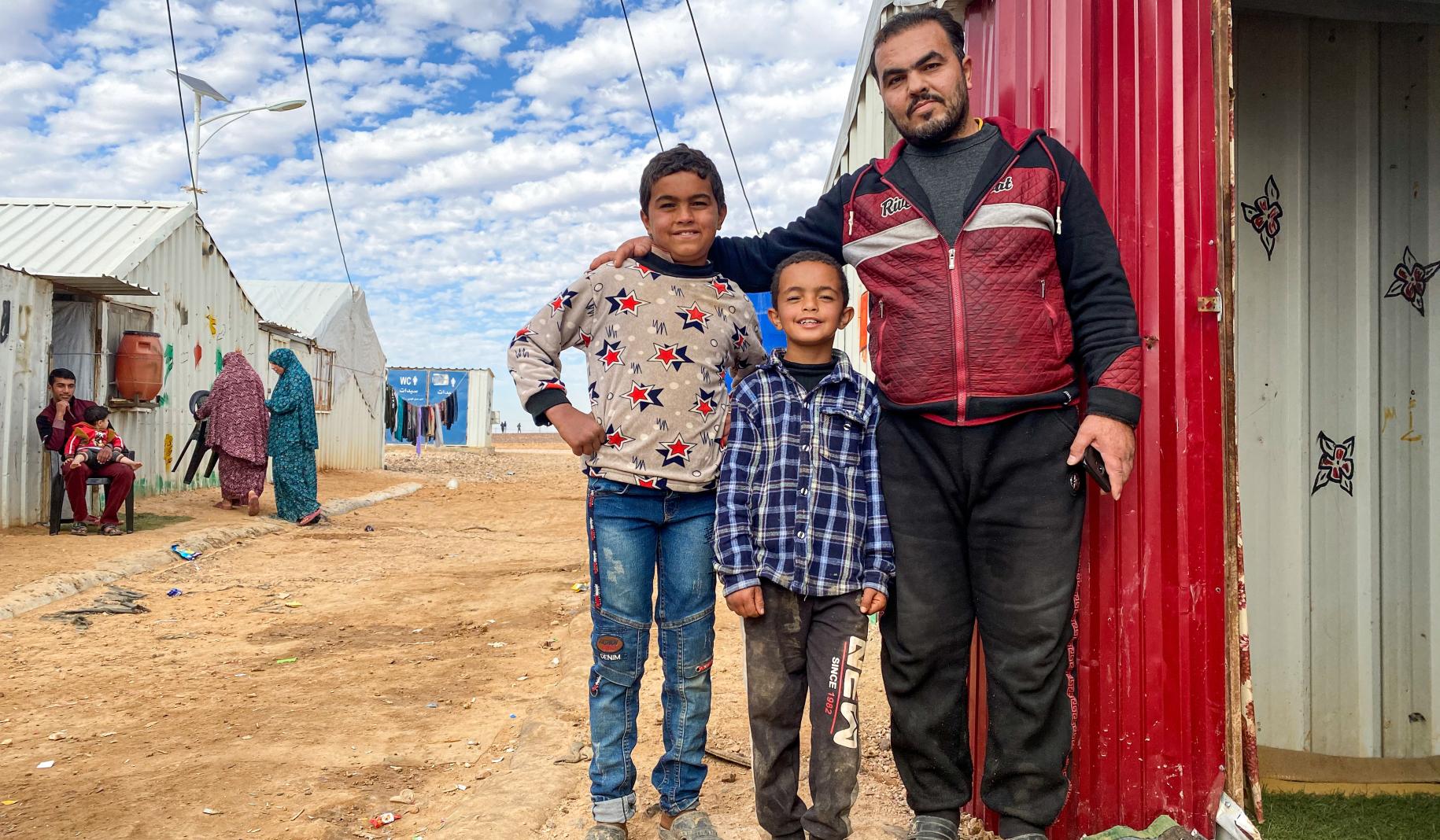 Ahmad proudly places his arms around his two young sons as they stand outside their home and pose for the camera.