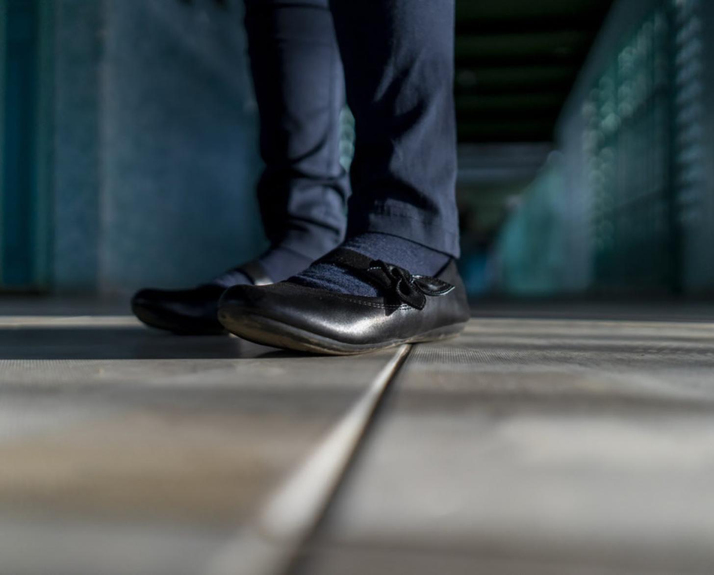 صورة مقرّبة لحذاء أسود ولباس مدرسي أزرق حتى الركبتين.