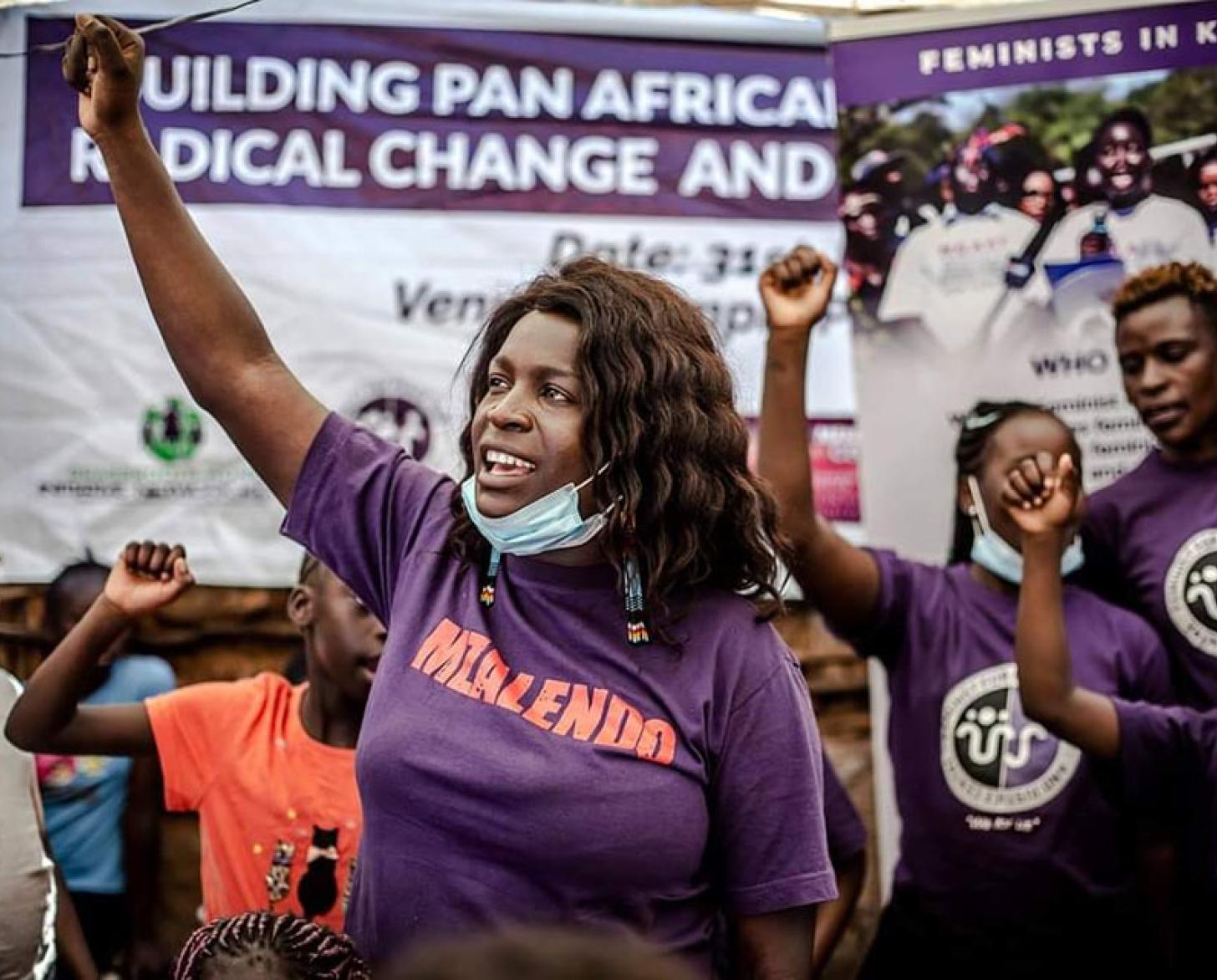 Une femme se tient devant un groupe de manifestants le bras et le poing levés.