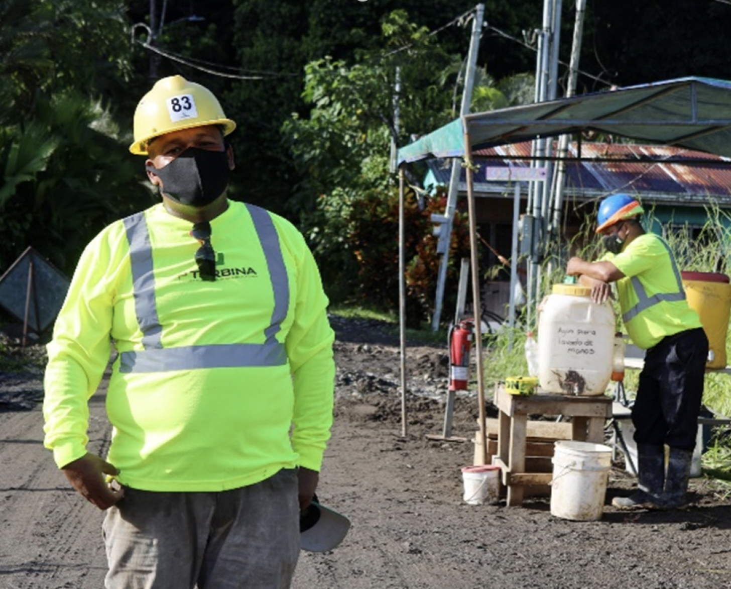 رجل يرتدي قميصًا أصفر وقبعة بناء صفراء ينظر إلى الكاميرا.