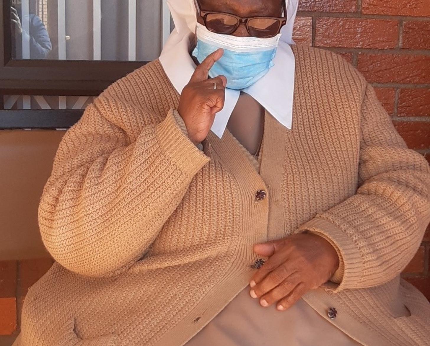 امرأة ترتدي سترة وثوبًا ترفع إحدى يديها بينما تضع يدها الأخرى على حجرها.