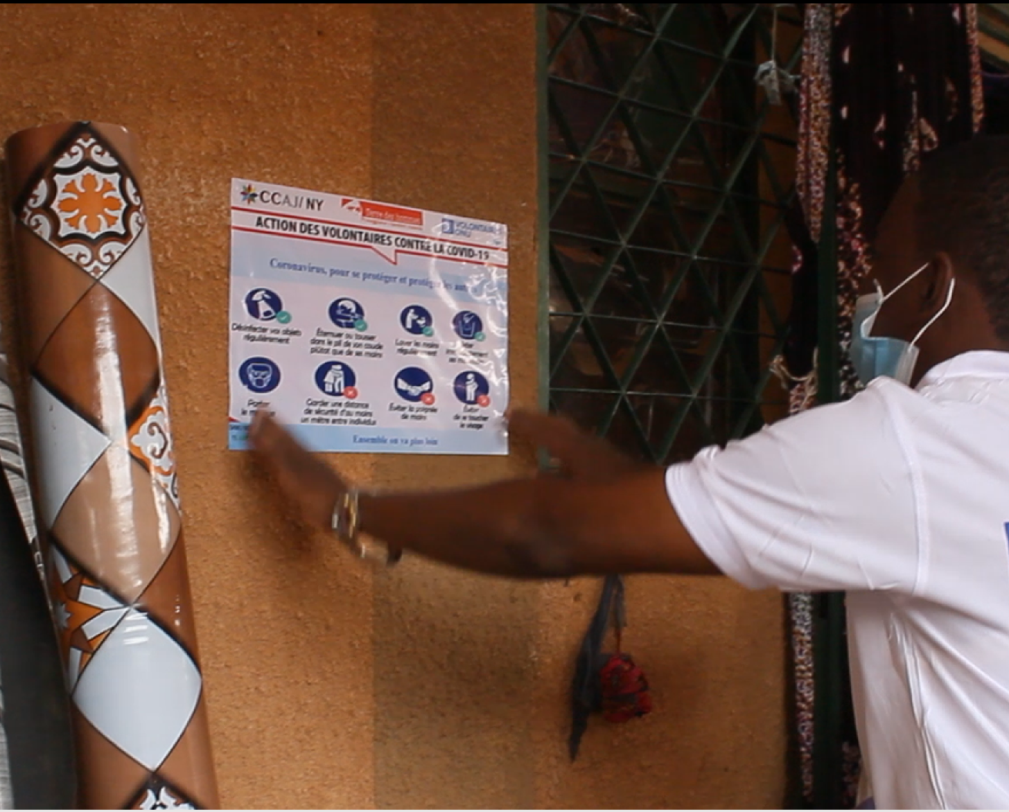 A person hangs a COVID-19 informational poster on a wall. 