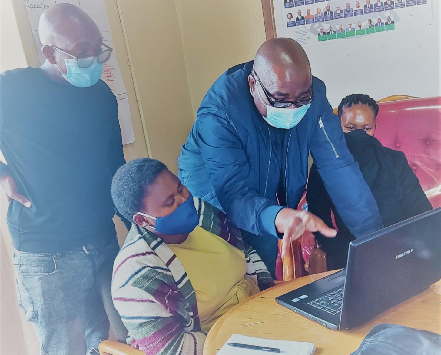 رجلان يقفان فوق شخصين يجلسان بجانب جهاز كمبيوتر.