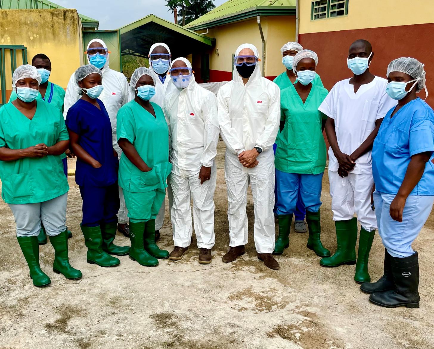 A large group of people in protective medical gear stand in a semi-circle looking at the camera. 