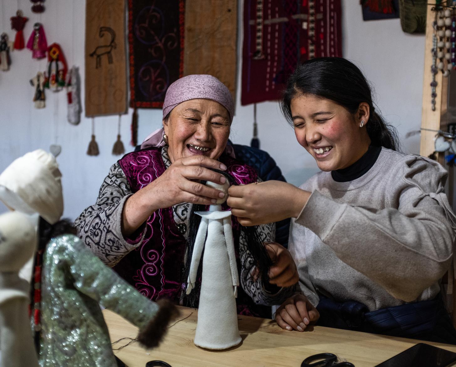 Two women smile while they put together a doll. 