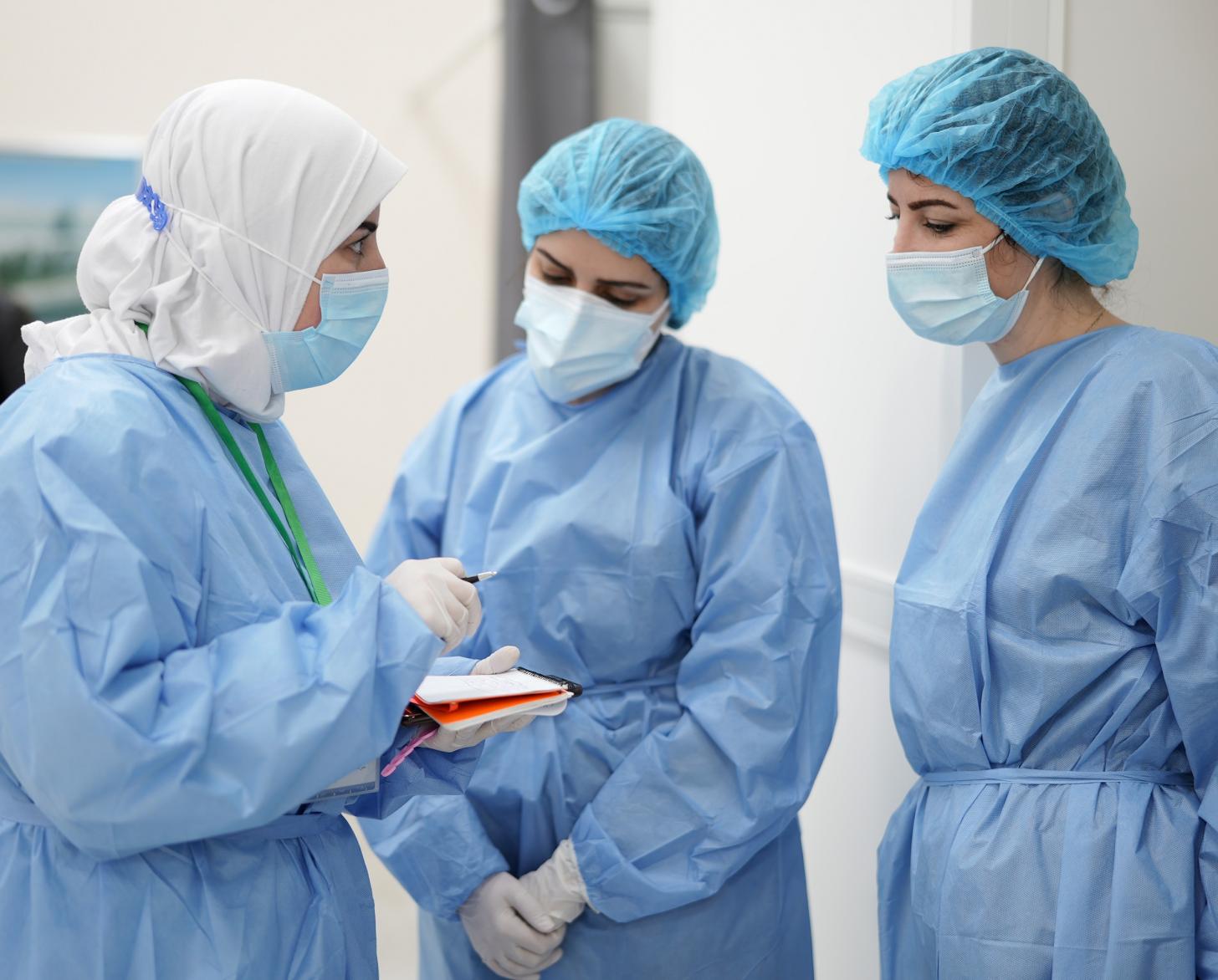 Three people dressed in medical equipment speak in a semi-circle. 