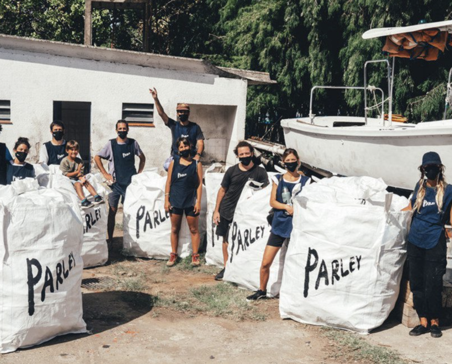 穿着蓝色衬衫和戴着口罩的人站在一艘船边的白色大袋子旁。