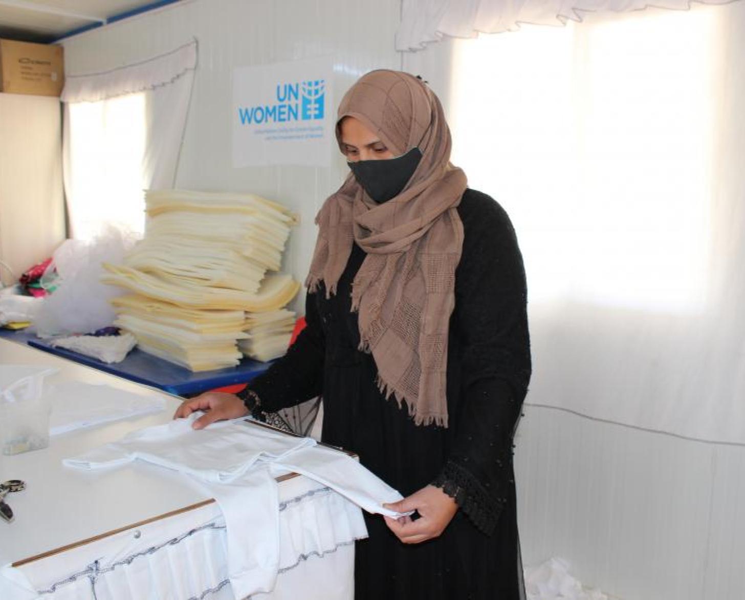 在绿洲中心的缝纫室里，诺法·阿里·沙德戴着口罩，仔细查看一件纯白的童装。